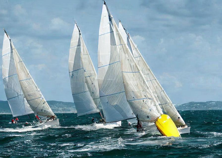 Sailboats racing tightly around yellow buoy on choppy ocean waters