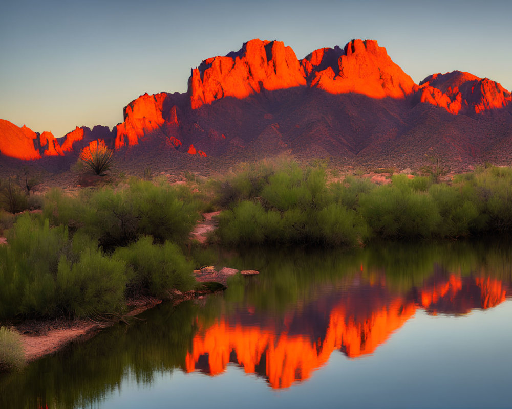 Vibrant sunset over mountain peaks, reflecting river, and desert vegetation.