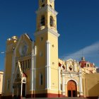 Stucco church with bell tower and cross against blue sky