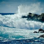 Dramatic stormy sea waves crashing against rocks under sunlight