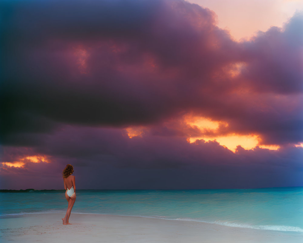 Person gazes at dramatic sky over beach at sunrise or sunset