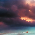 Person gazes at dramatic sky over beach at sunrise or sunset