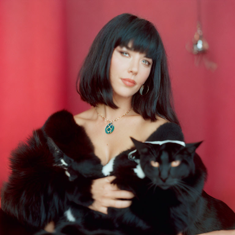 Woman with Black Bob Haircut in Fur Coat Holding Black Cat on Red Background