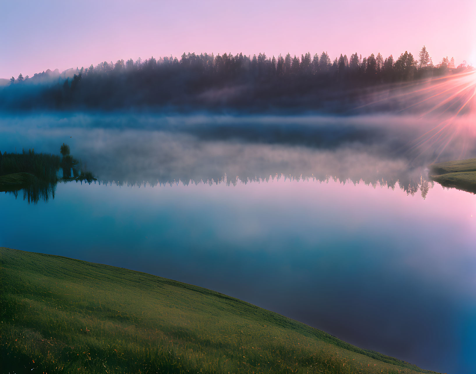 Tranquil sunrise scene over misty lake with tree reflections.