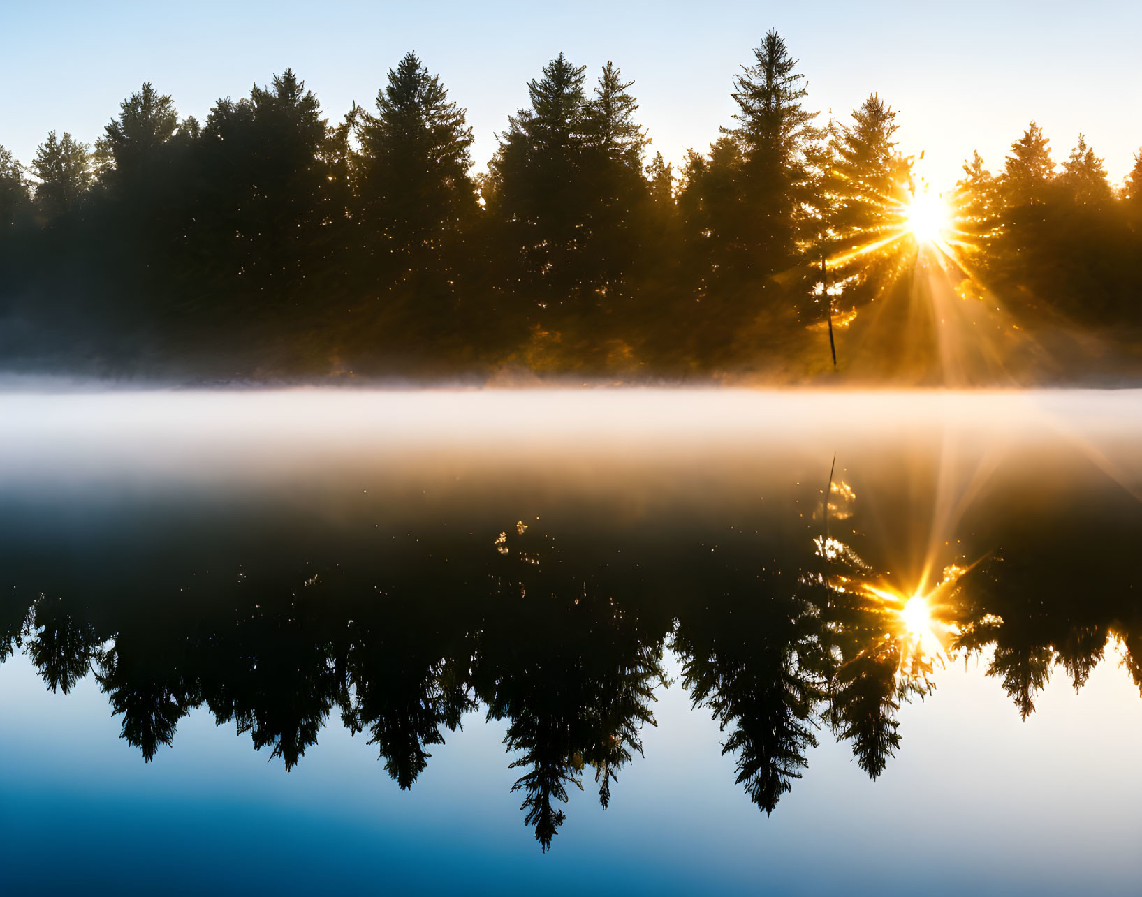 Scenic sunrise over tranquil lake with mist and mirrored reflection
