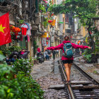 Vietnamese flag in vibrant street scene with cobblestone path, train tracks, red umbrellas,