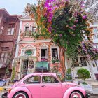 Pink vintage car parked in front of quaint house with vibrant flowers