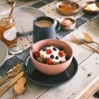 Breakfast scene with cereal, berries, coffee, nuts, and book on wooden surface