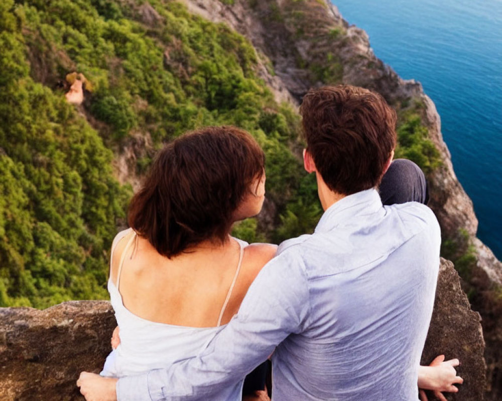 Couple sitting on scenic cliff with lush greenery and blue sea