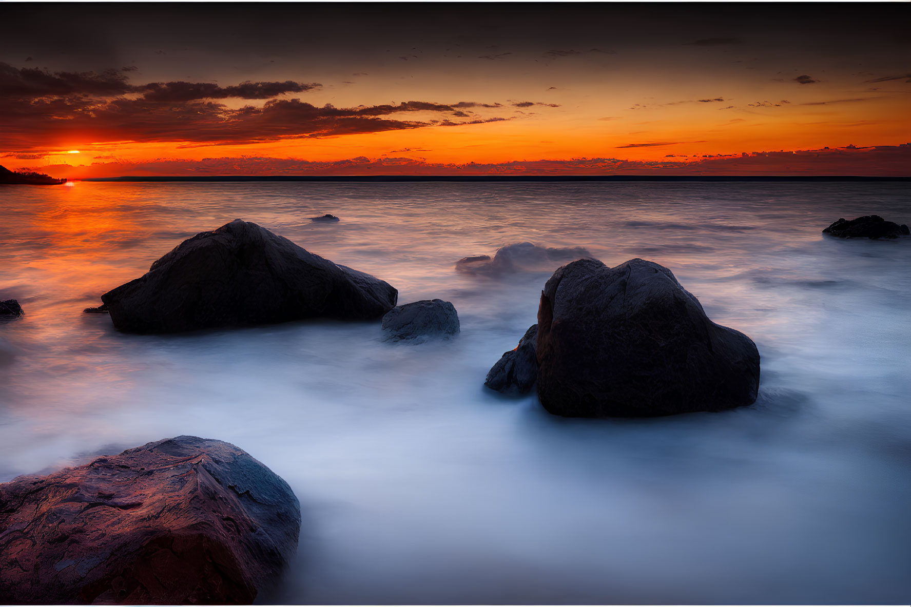 Tranquil sunset scene with orange hues over calm sea and silhouetted rocks