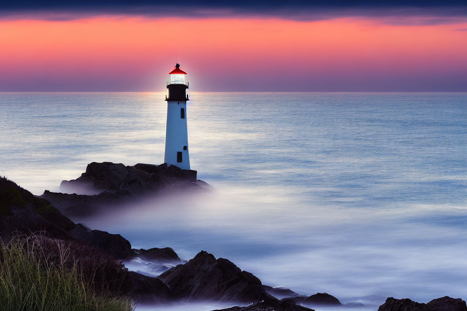 Tranquil seascape with white lighthouse, misty ocean, and colorful sunset sky