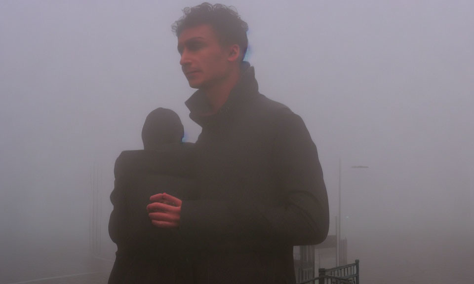 Person in dense fog wearing warm jacket and looking contemplative.