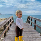 Child in white shirt and yellow boots on wooden pier by calm sea