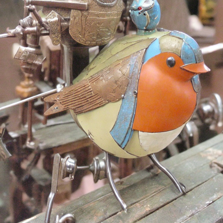 Colorful Metal Bird Sculpture with Tiny Bird on Back Amid Rustic Gears