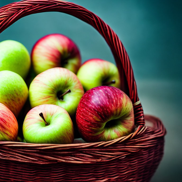 Fresh multicolored apples in wicker basket on teal background